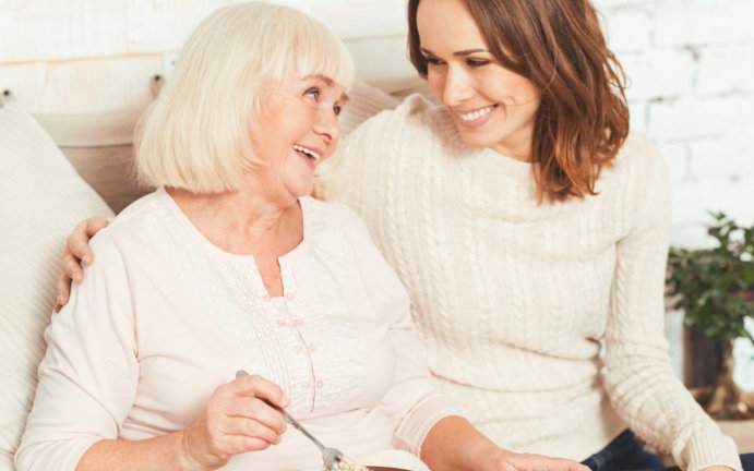 a caregiver and a senior woman looking at each other while smiling